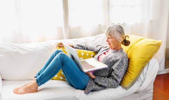 Woman using laptop on couch in sunny room