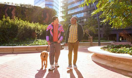 2 Black men walk a labrador retriever outside